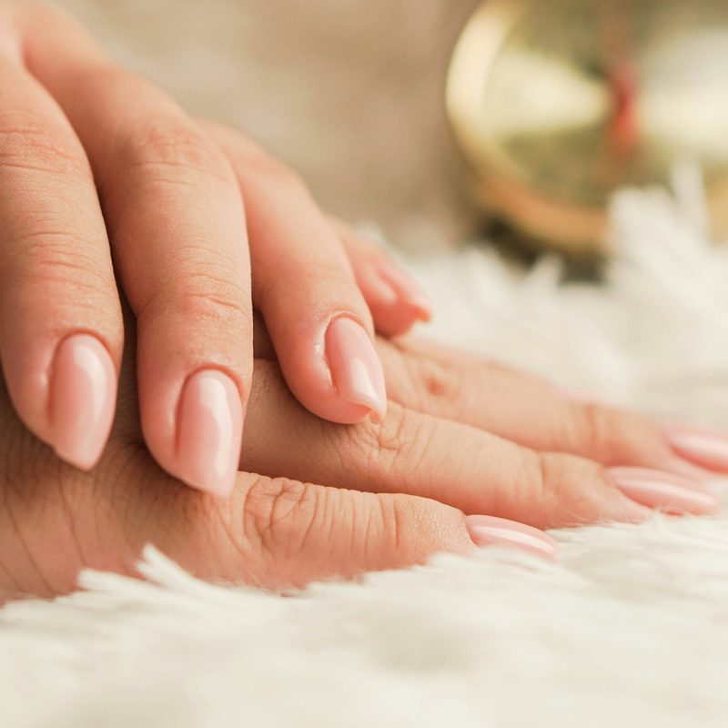 Hands applying cuticle oil after manicure with nail art tools nearby