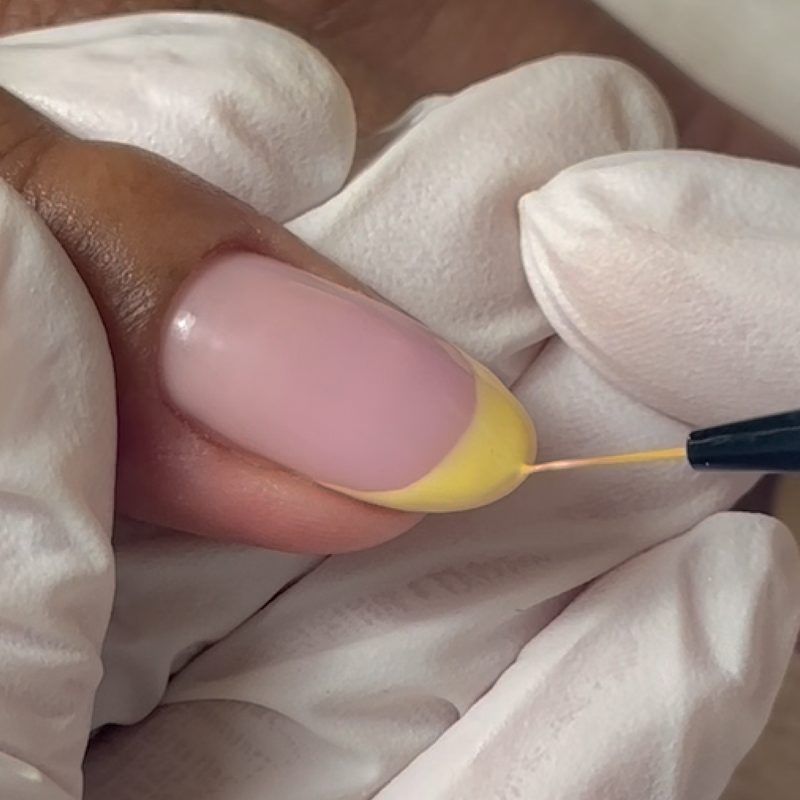 Hands using a nails art brush liner to paint fine lines on nails
