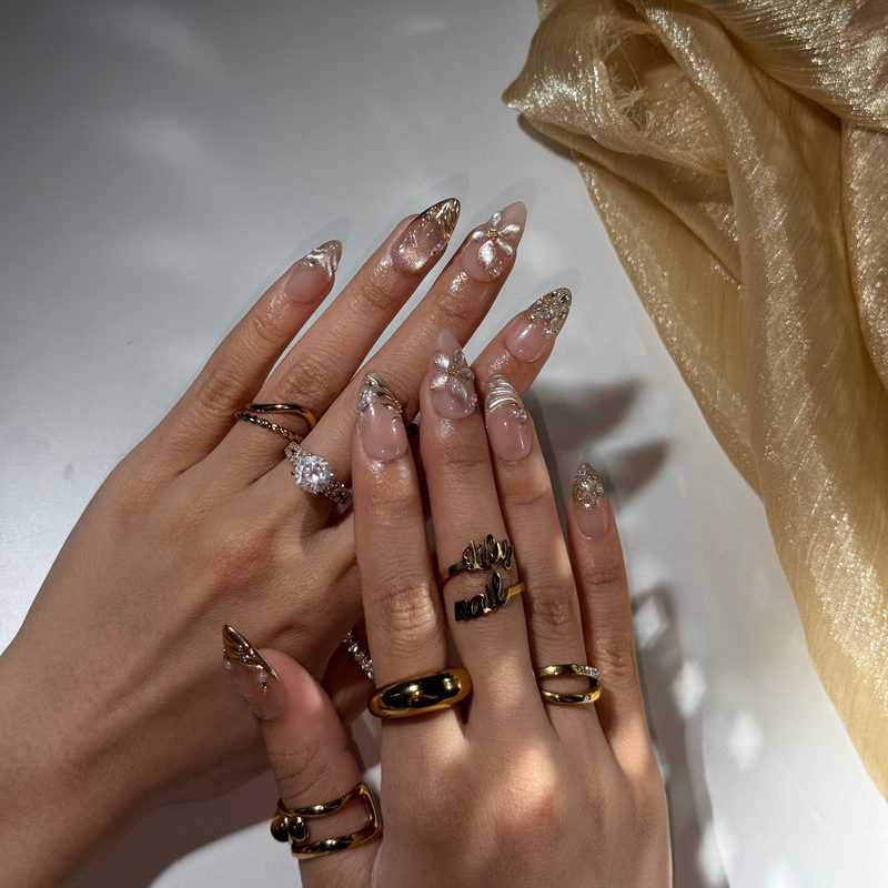 Nail art featuring pen designs combined with foil accents and small gems for texture