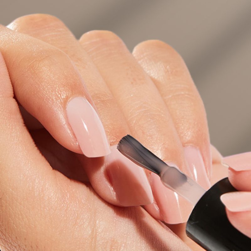 nail artist applying gel polish with professional brush and lamp