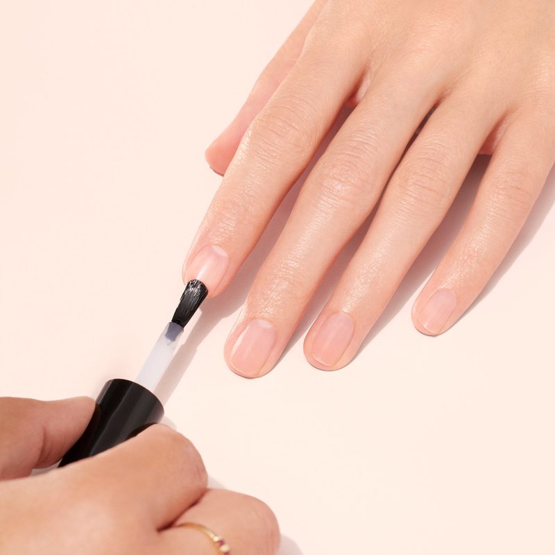 Hand applying nail art base coat with brush on natural nails